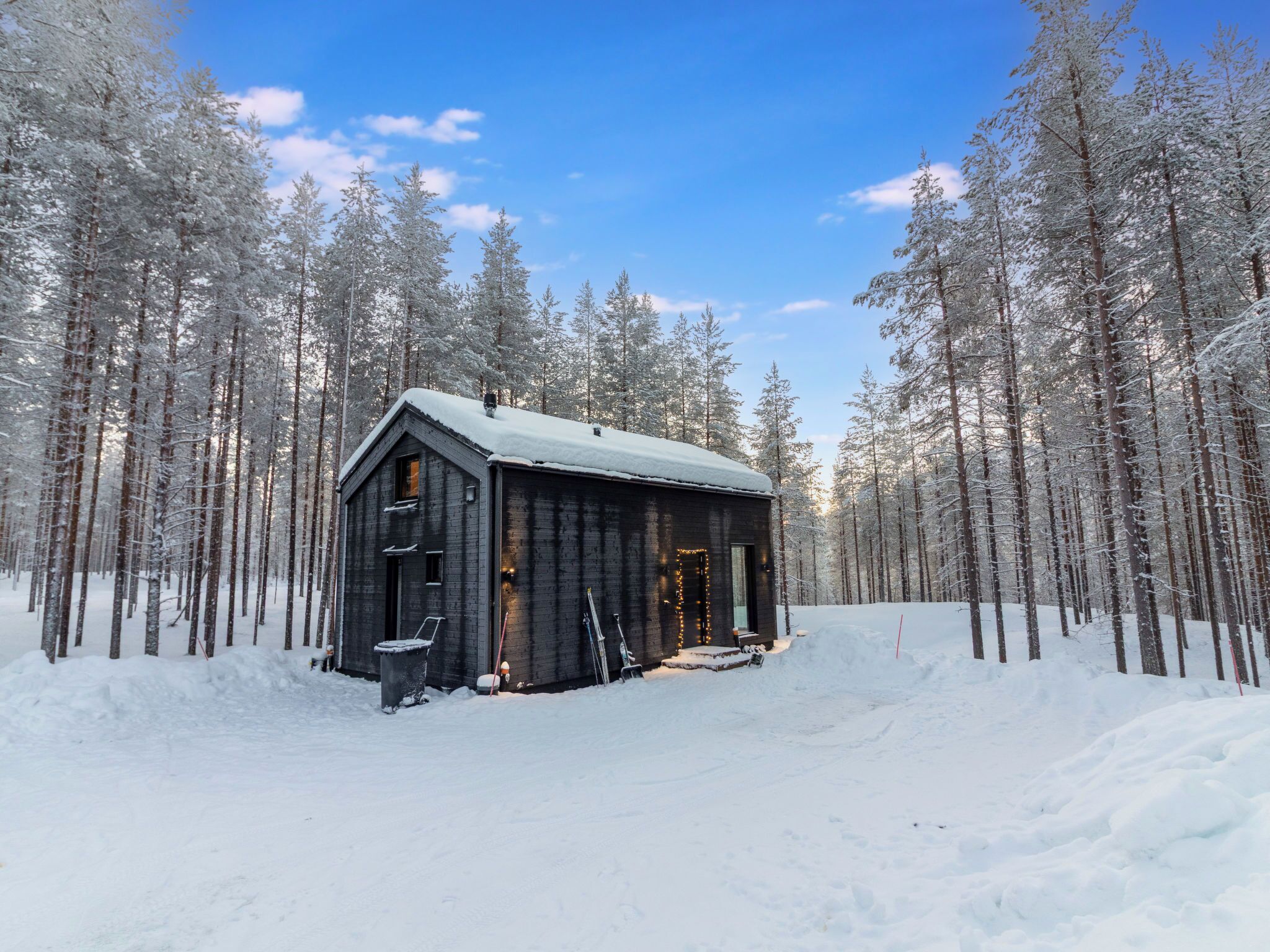 Une cabane au cœur d’une forêt enneigée, sous un ciel dégagé.