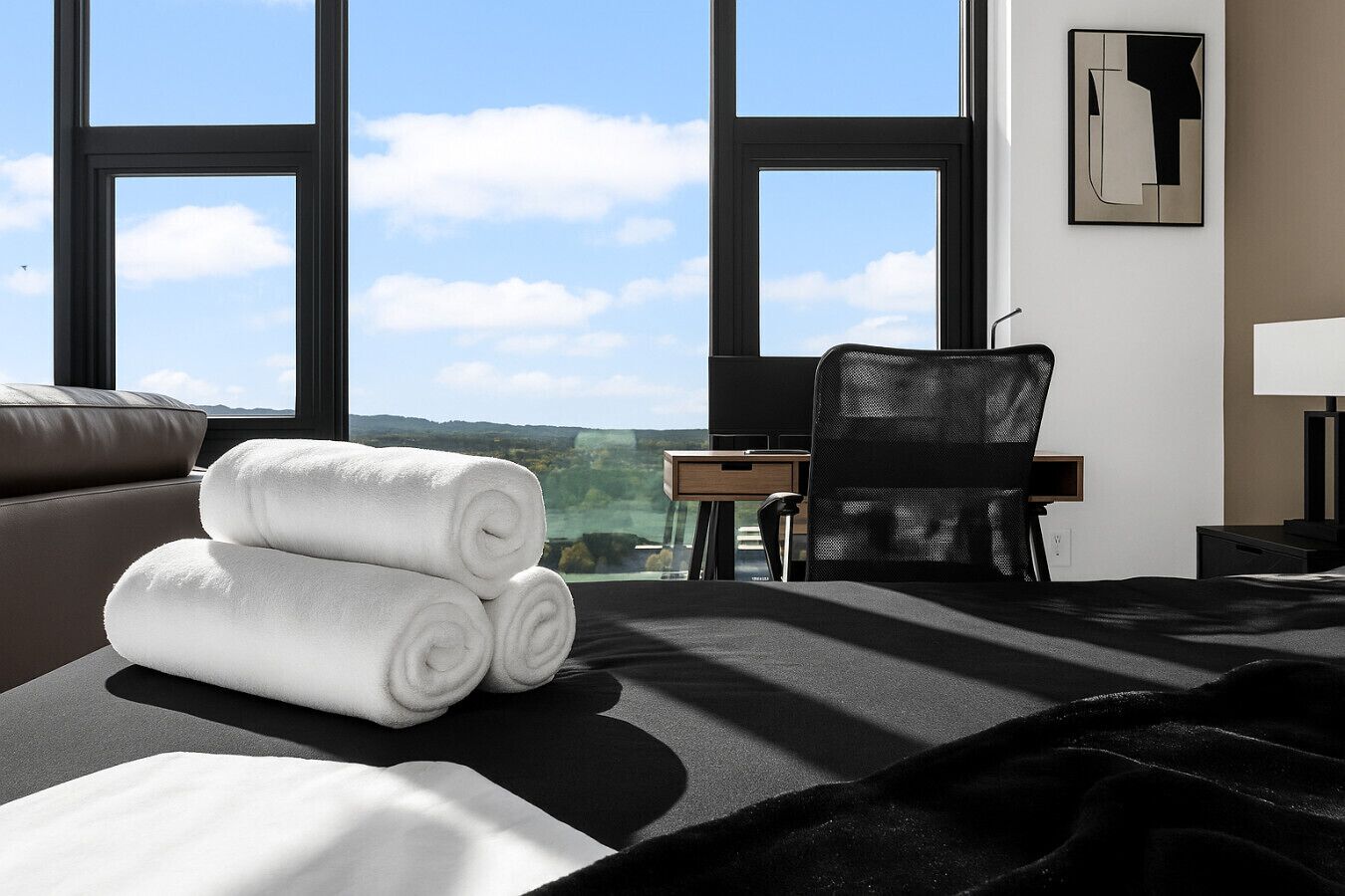 A hotel room with a large window, a bed, a chair, and a desk.