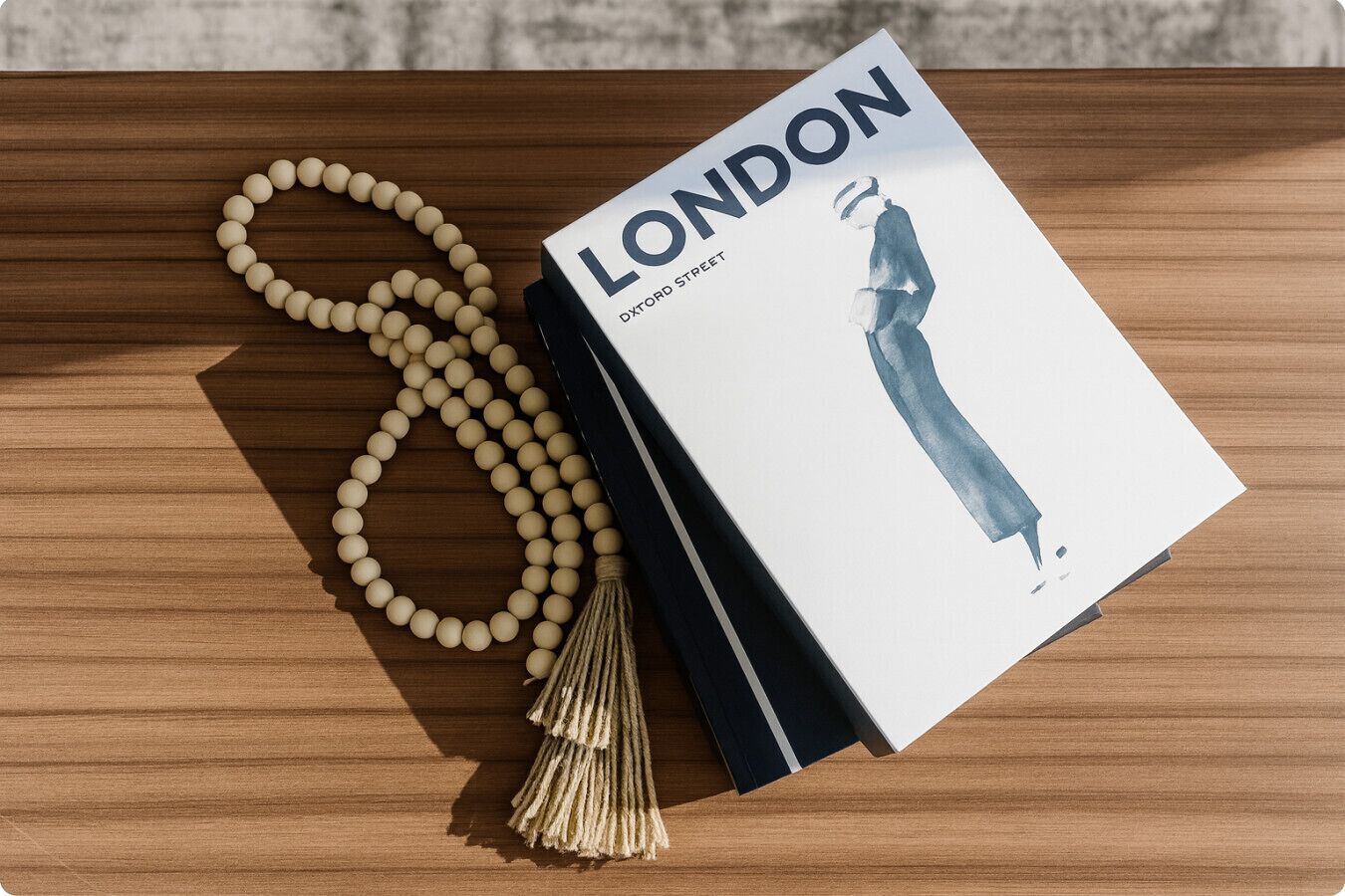 Un livre intitulé « LONDON » est posé sur une surface en bois, accompagné d’un collier de perles et d’une frange.