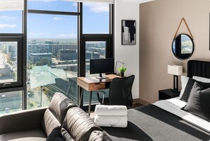 A modern hotel room with a large window offering a city view, a desk with a computer, a comfortable bed, and a bedside table with a lamp. - Cozy Urban Hideaway in Birmingham 10 (Birmingham)