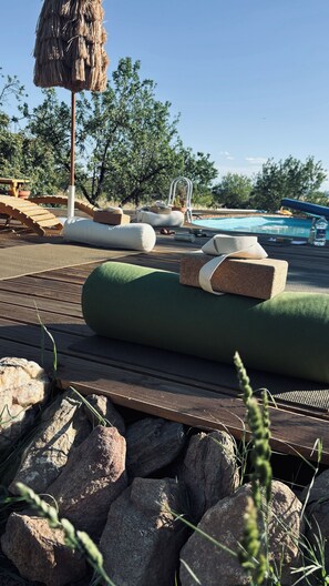 Un espace aménagé au bord de la piscine, avec des chaises longues, une terrasse en bois et un parasol en chaume.