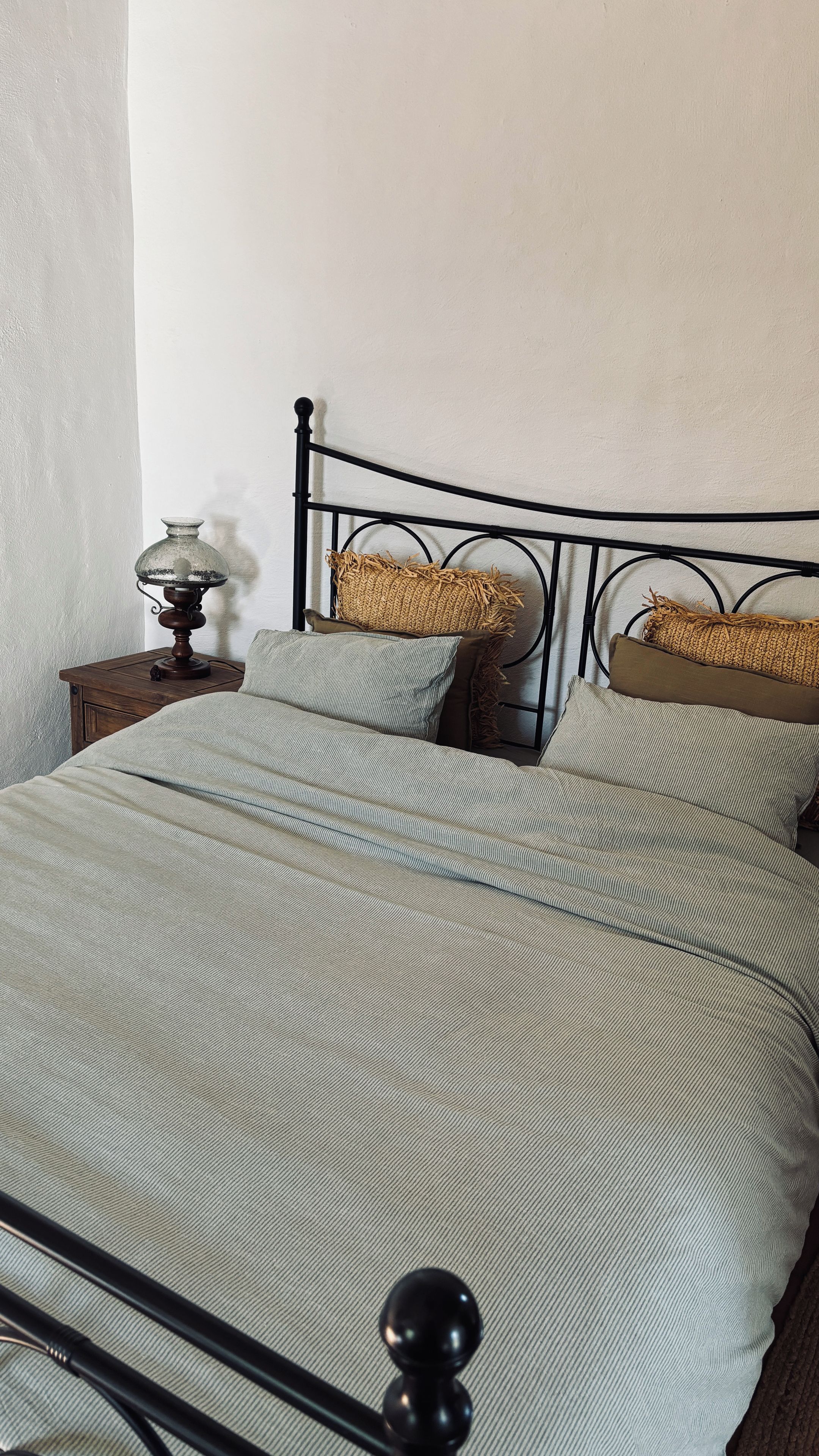 A bed with a metal frame, a wooden nightstand with a lamp, and two pillows.