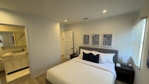 A bedroom with a large bed, a nightstand, a dresser, and a bathroom with a mirror and sink. - Contemporary 2 Bedroom 2 Bath in Beautiful Neighborhood (Los Angeles)