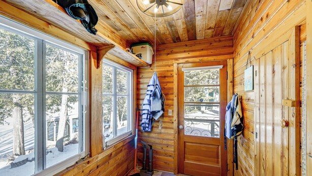 L’intérieur d’une cabane en bois, avec de grandes fenêtres, une porte et un ventilateur de plafond.