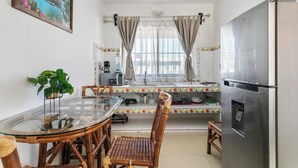 A compact kitchen with a glass dining table, wooden chairs, a stainless steel refrigerator, and a window with curtains. - Luna de Plata (Playa del Carmen)