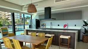 Une cuisine moderne dotée d’un îlot central, un coin repas avec une table en bois et des chaises jaunes, et une grande fenêtre offrant une vue sur la ville.