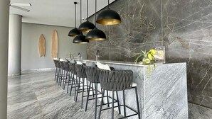Un espace bar moderne doté d’un comptoir en marbre, de tabourets de bar noirs et de luminaires suspendus.