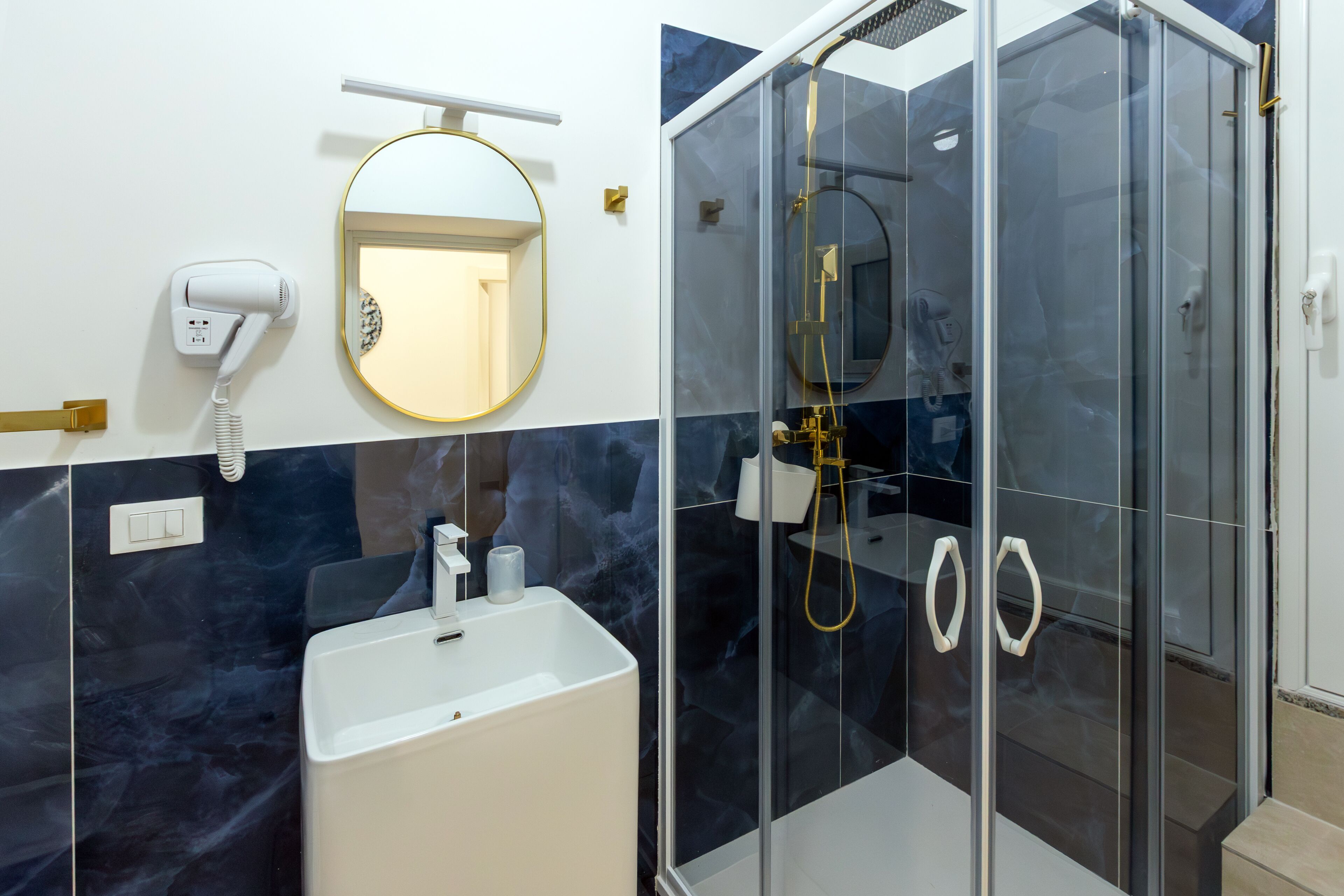 Un baño moderno con ducha de vidrio, lavamanos blanco, secador de pelo y espejo.