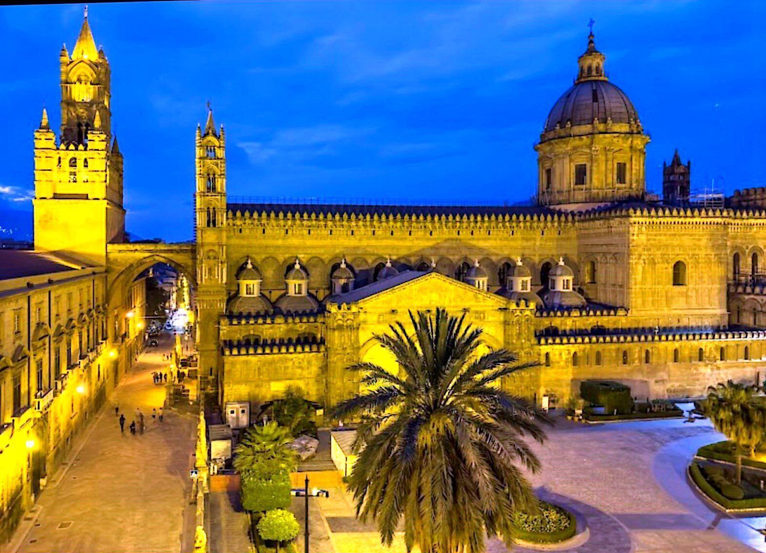 A historic building with a prominent clock tower and a large dome, surrounded by a well-maintained courtyard with palm trees.