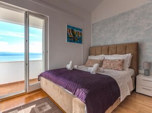 A bedroom with a bed, a nightstand, a painting, and a view of the sea. - Seven Bedroom Villa with Outdoor Pool (Stanici)