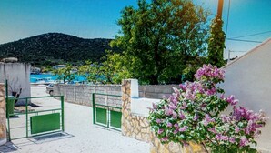Ein Innenhof mit einer Steinmauer, einem grünen Tor und einem blühenden Strauch.