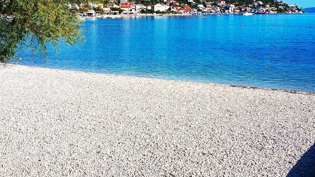 Eine Küstenstadt mit Kiesstrand, klarem blauen Wasser und Häusern an einem Hügelhang.