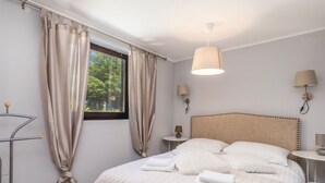 Ein ordentlich bezogenes Bett mit Kopfteil, zwei Nachttische mit Lampen und ein Fenster mit Vorhängen.