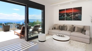 Een moderne woonkamer met een grote schuifpui naar een balkon, een beige bank, een salontafel en een schilderij van een zonsondergang.