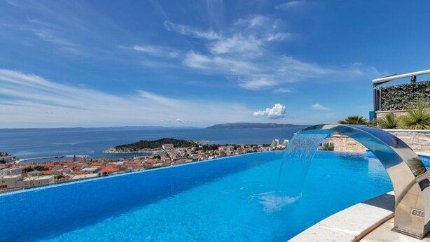 A swimming pool with a waterfall feature, overlooking a coastal town with buildings and a clear blue sky. - Lux Villa Afrodita Makarska - Three Bedoom Villa with Outdoor Pool (Makarska)