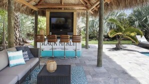 A covered outdoor seating area with a sofa, bar stools, and a television screen. - Swimming Pool / Boat Dock / Close to Key West (Sugarloaf)