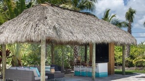 A thatched-roof outdoor seating area with a pool, surrounded by palm trees. - Swimming Pool / Boat Dock / Close to Key West (Sugarloaf)