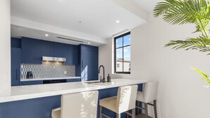 Une cuisine moderne avec un plan de travail blanc, des armoires bleues et une fenêtre qui laisse entrer la lumière naturelle.