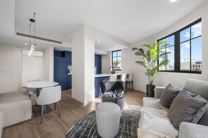 A modern living room with a grey sofa, a round coffee table, and a dining area with a white table and chairs.