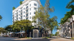 Un hôtel à plusieurs étages, doté de balcons, d’une façade incurvée et donnant sur la rue, où l’on peut voir des voitures garées et des arbres.