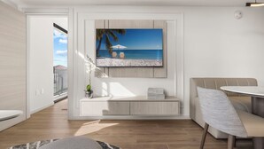 Un salon moderne avec un grand téléviseur à écran plat fixé au mur, un coin salon comprenant un canapé et une table ronde, ainsi qu’une petite plante en pot posée sur une console.