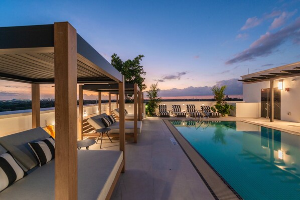 A rooftop pool area with lounge chairs and a pergola.