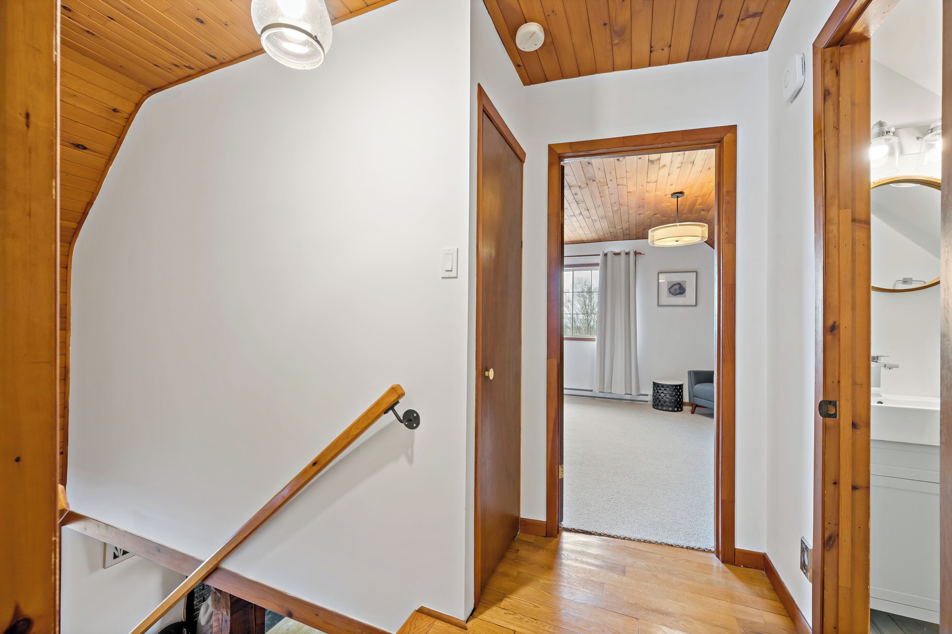 Una escalera de madera con barandilla que conduce a una habitación con techo blanco y vigas de madera.