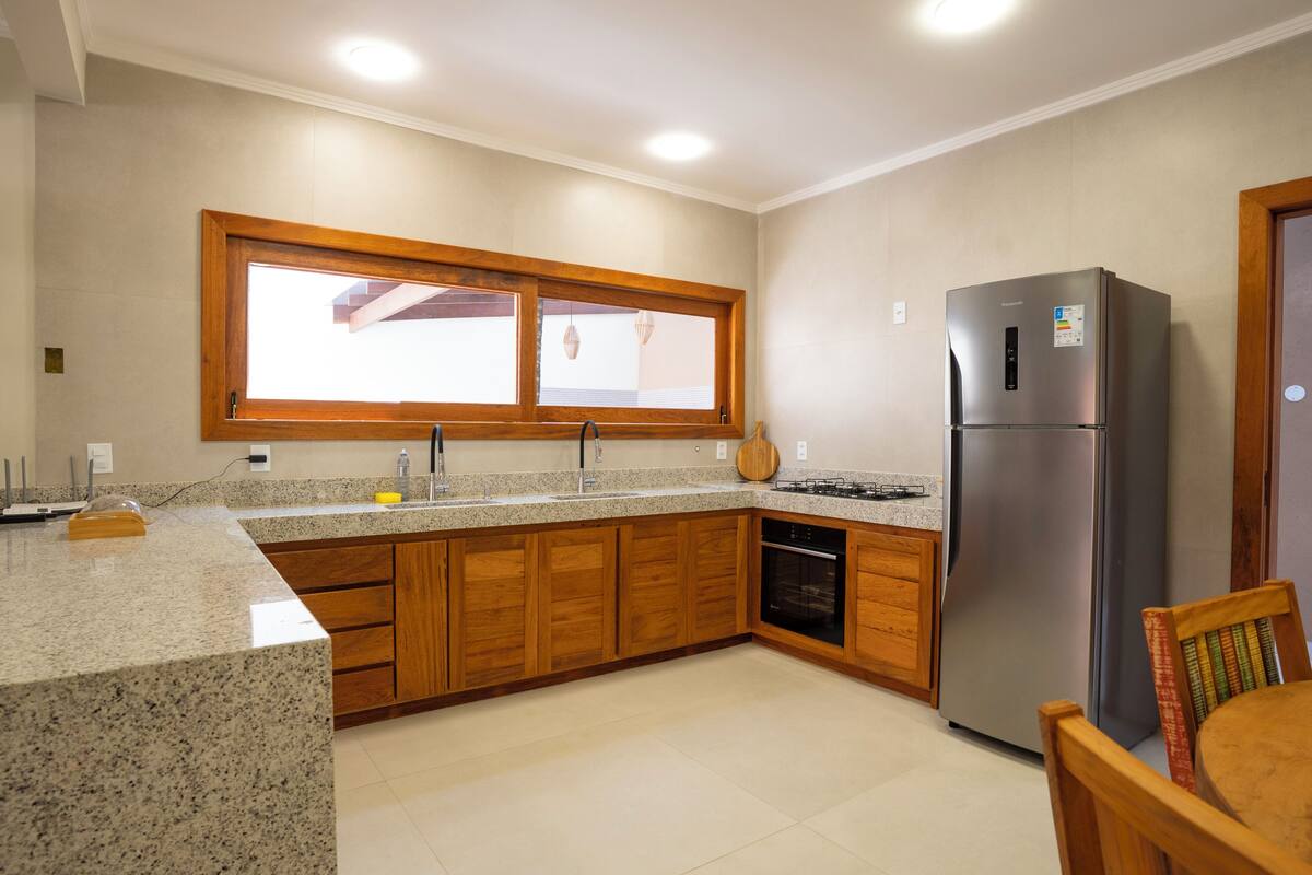 A kitchen with wooden cabinets, a built-in oven, a stainless steel refrigerator, and a window above the sink.