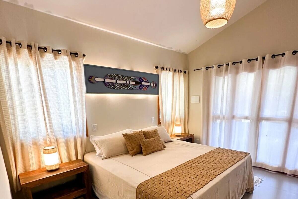 A bedroom with a large bed, bedside tables, a hanging light fixture, and curtains.