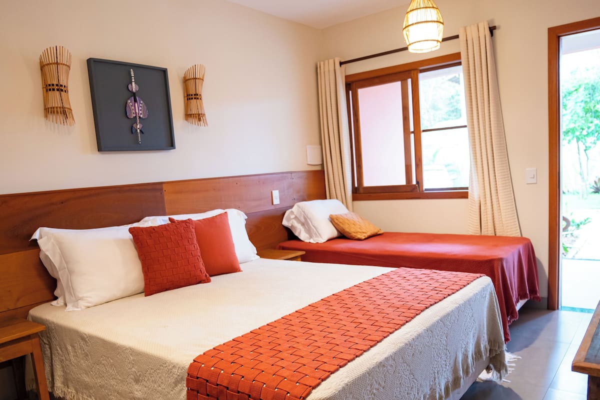 A hotel room with a large bed, a smaller bed, a wooden headboard, a window with curtains, and a wall-mounted light fixture.