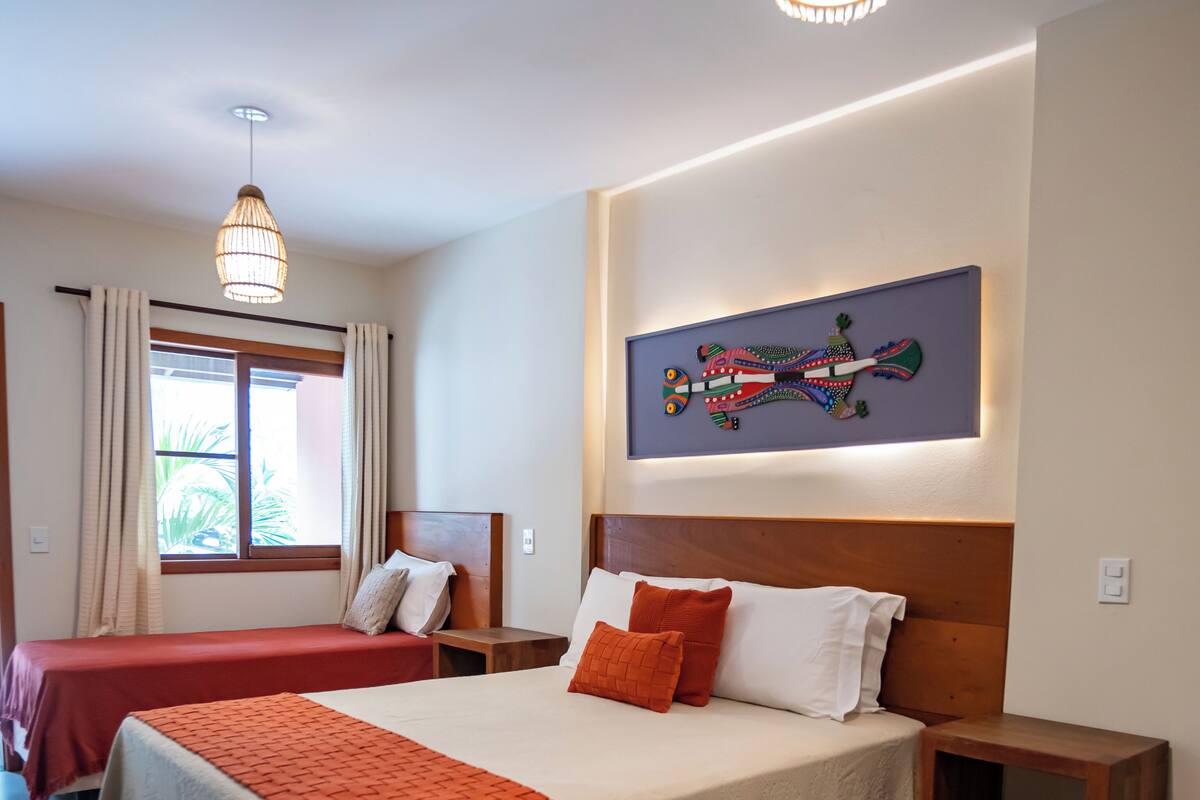 A modern hotel room with a large bed, a smaller bed, a nightstand, a wall-mounted artwork, and a window with curtains.