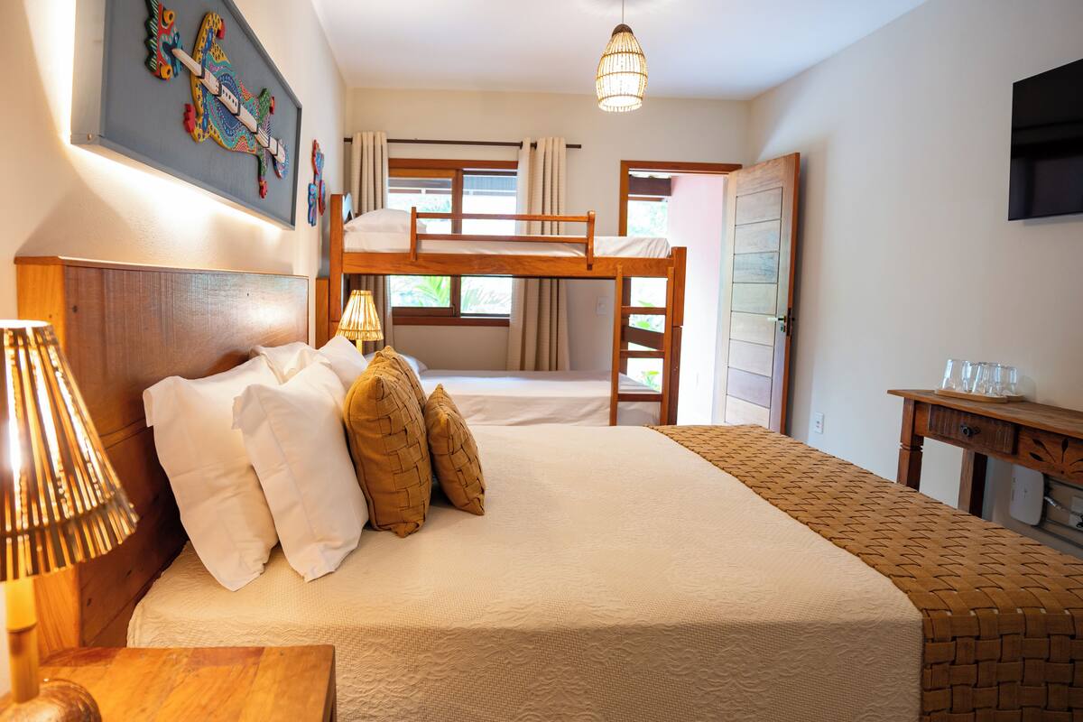A bedroom with a bunk bed, a bedside table with a lamp, a bed with pillows, a small table with glasses, and a painting on the wall.
