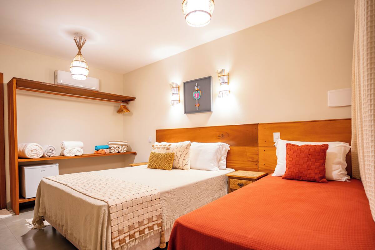 A hotel room with a large bed, a smaller bed, a desk with a chair, a wardrobe, and a ceiling fan.