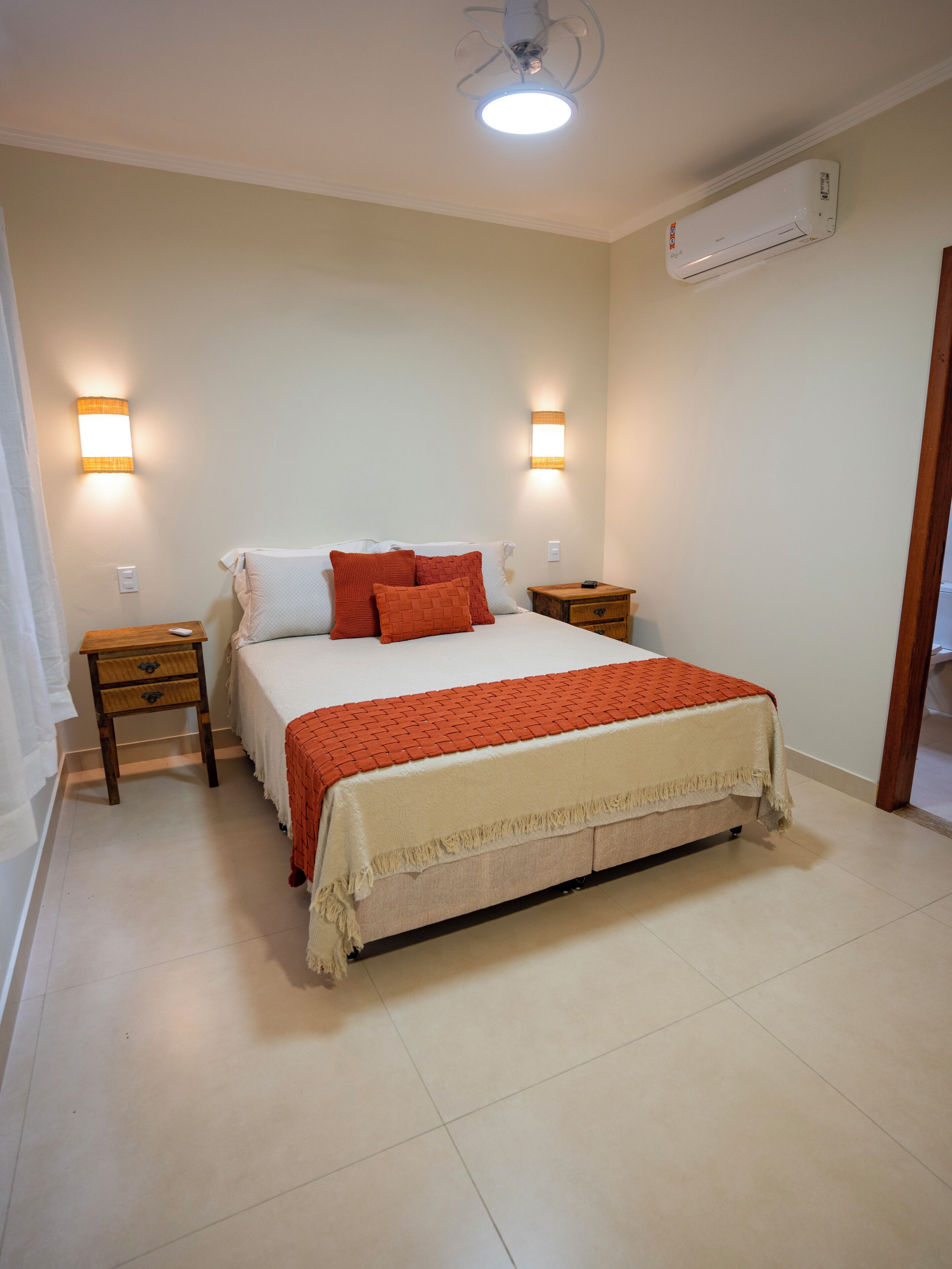 Un dormitorio con una cama, dos mesitas de noche, un aire acondicionado de pared y un ventilador de techo.