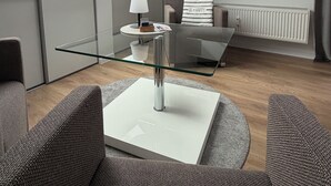 Ett modernt vardagsrum med ett soffbord i glas, grå soffor, en platt-tv som är monterad på väggen och takfönster.