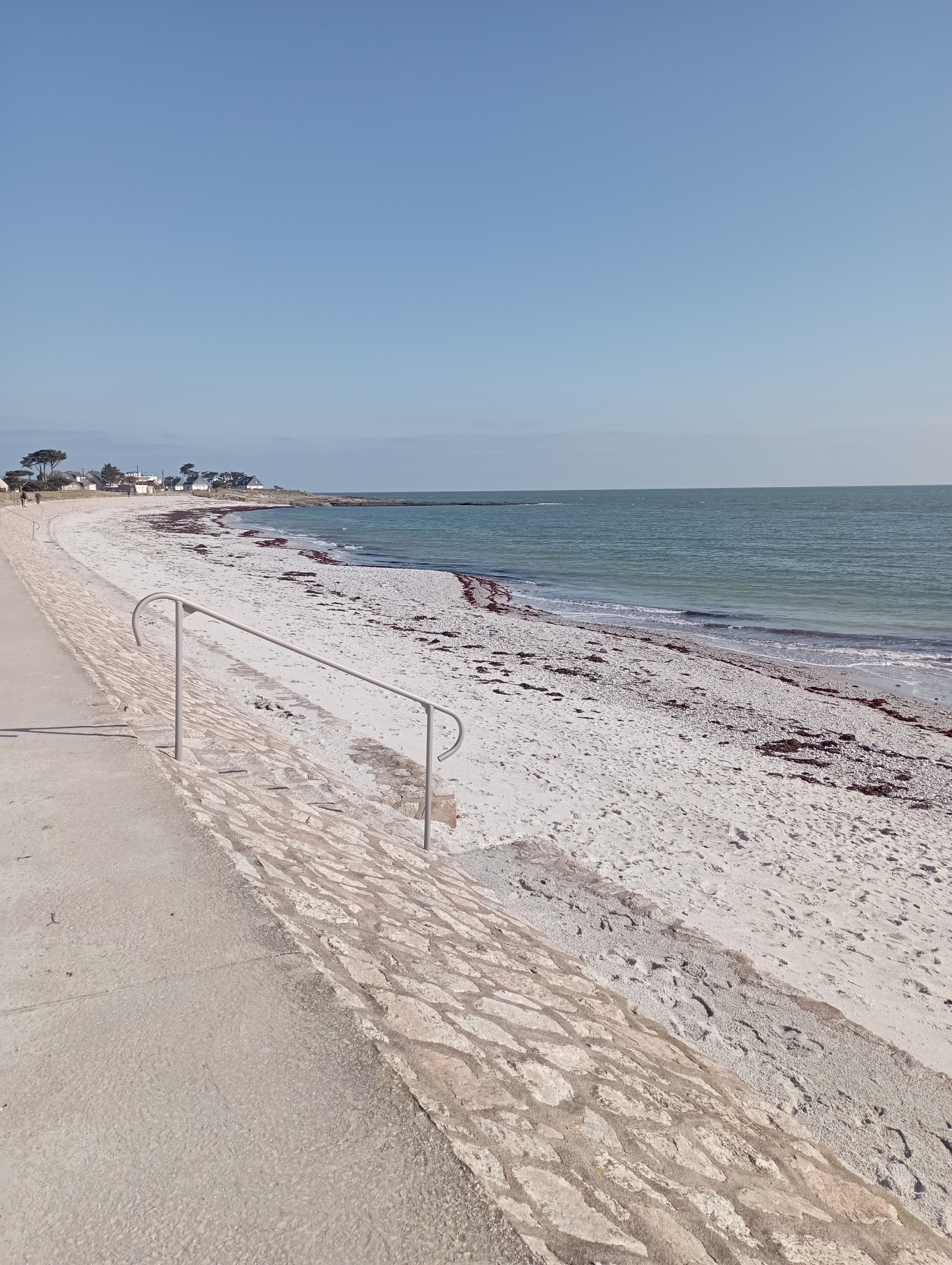 A beach with a concrete walkway and metal railing.