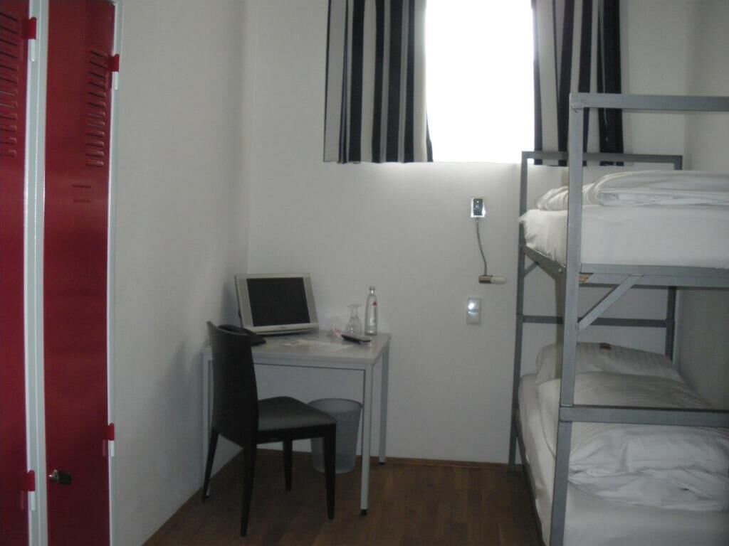 Una habitación pequeña con una cama litera, un escritorio con una computadora portátil, una silla y una ventana con cortinas.