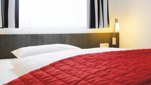 A hotel room with a bed, a nightstand with a lamp, and a window with curtains. - ALCATRAZ Hotel am Japanischen Garten (Kaiserslautern)