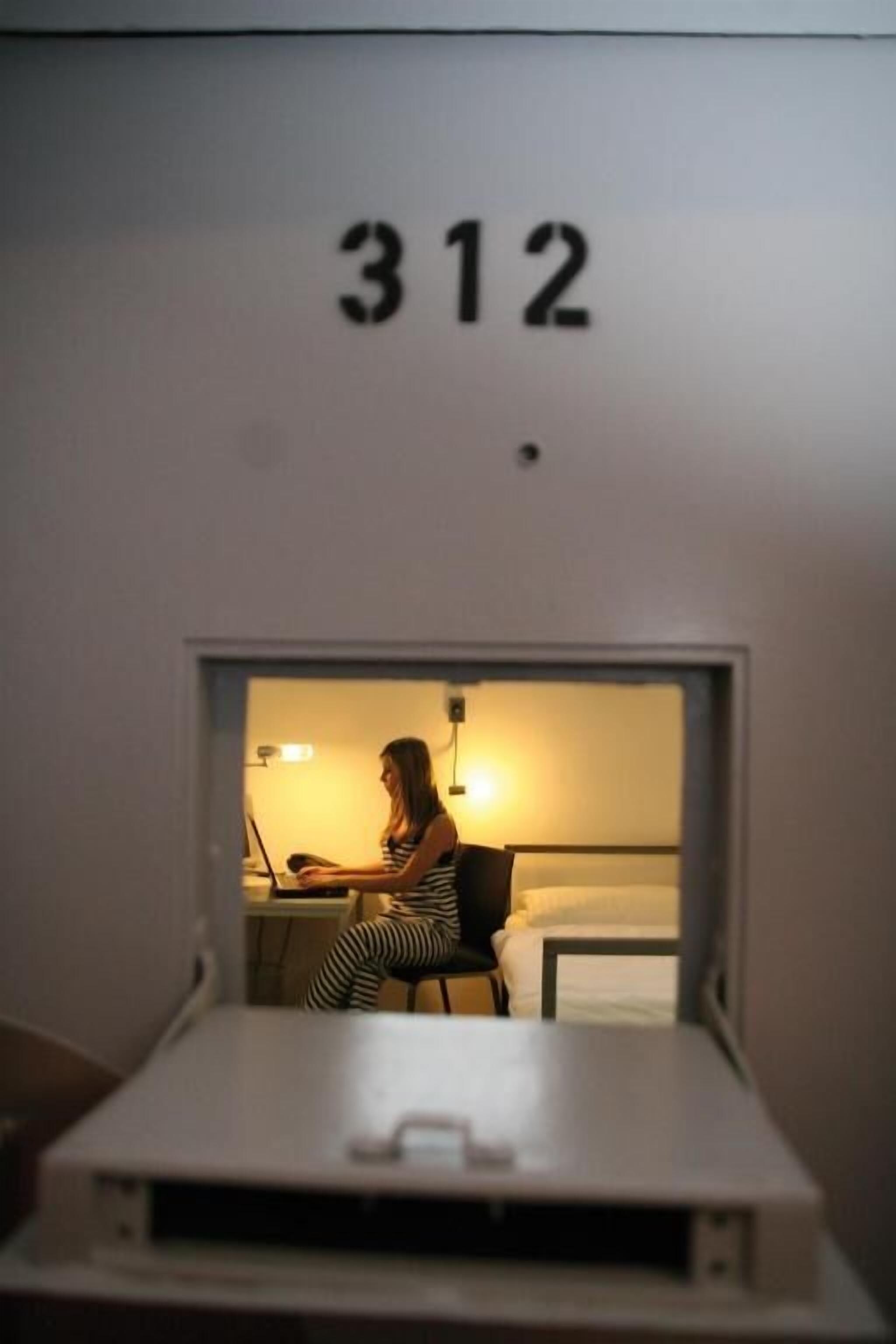 A room with a bed, a desk, and a person working on a laptop. The room number is 312.