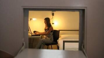 A room with a bed, a desk, and a person working on a laptop. The room number is 312.