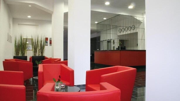 A modern lobby with red seating, a reception desk, and a staircase. - ALCATRAZ Hotel am Japanischen Garten (Kaiserslautern)
