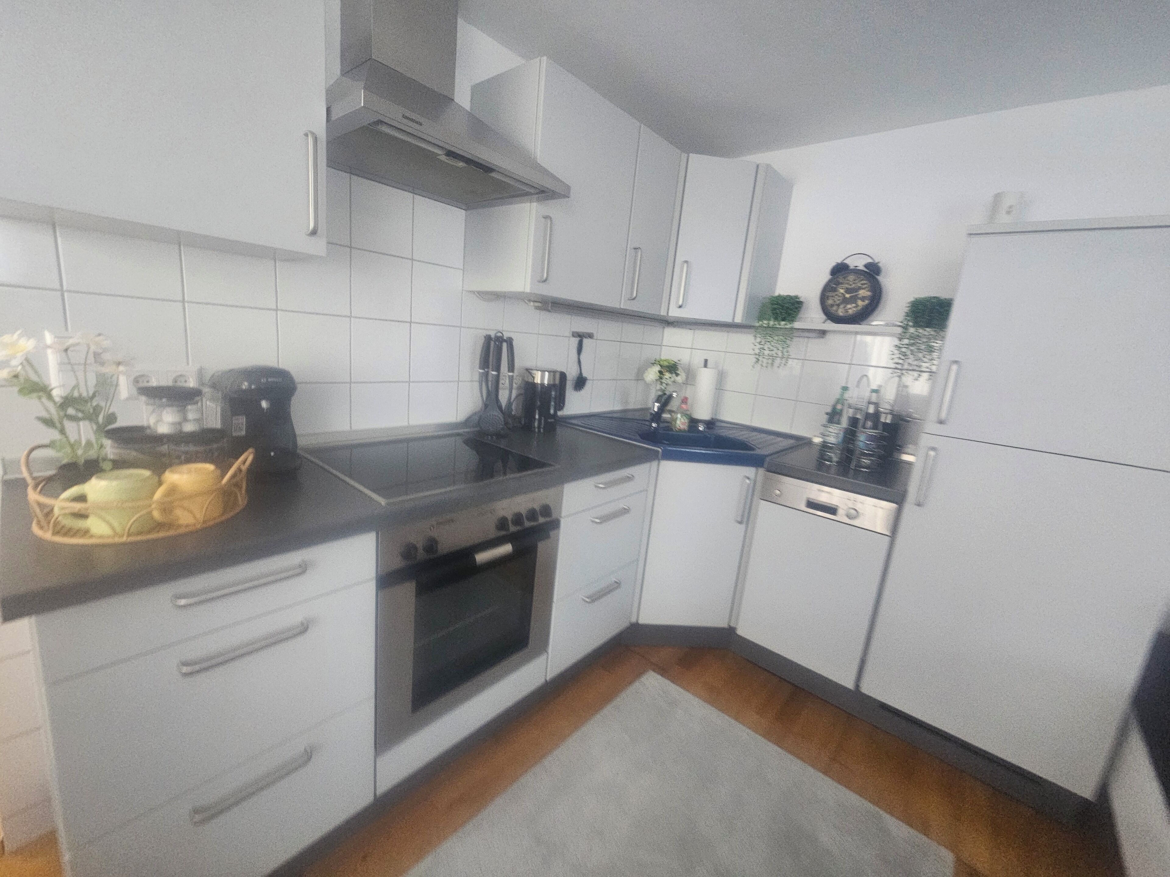 Une cuisine avec des meubles blancs, une cuisinière, un évier et un réfrigérateur.