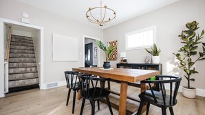 A dining area with a wooden table and black chairs, a chandelier, and potted plants.