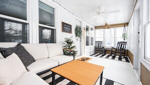 A white porch with a sofa, a wooden table, and chairs. A sign reads "Welcome to Porch."