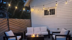 An outdoor seating area with a fire pit, string lights, and a patterned rug.