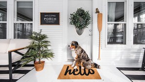 A porch with a dog, a welcome sign, a potted plant, and a wooden paddle.