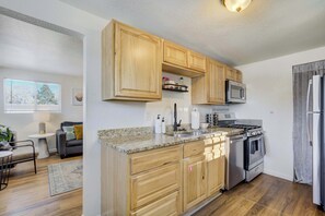 A modern kitchen with wooden cabinets, granite countertops, stainless steel appliances, and a dining area with a grey sofa and a small table. - Prospect Estate! Duplex Steps to Memorial Park (Colorado Springs)