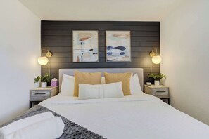 Un dormitorio moderno con una cama grande, dos mesitas de noche con lámparas y arte abstracto en la pared.