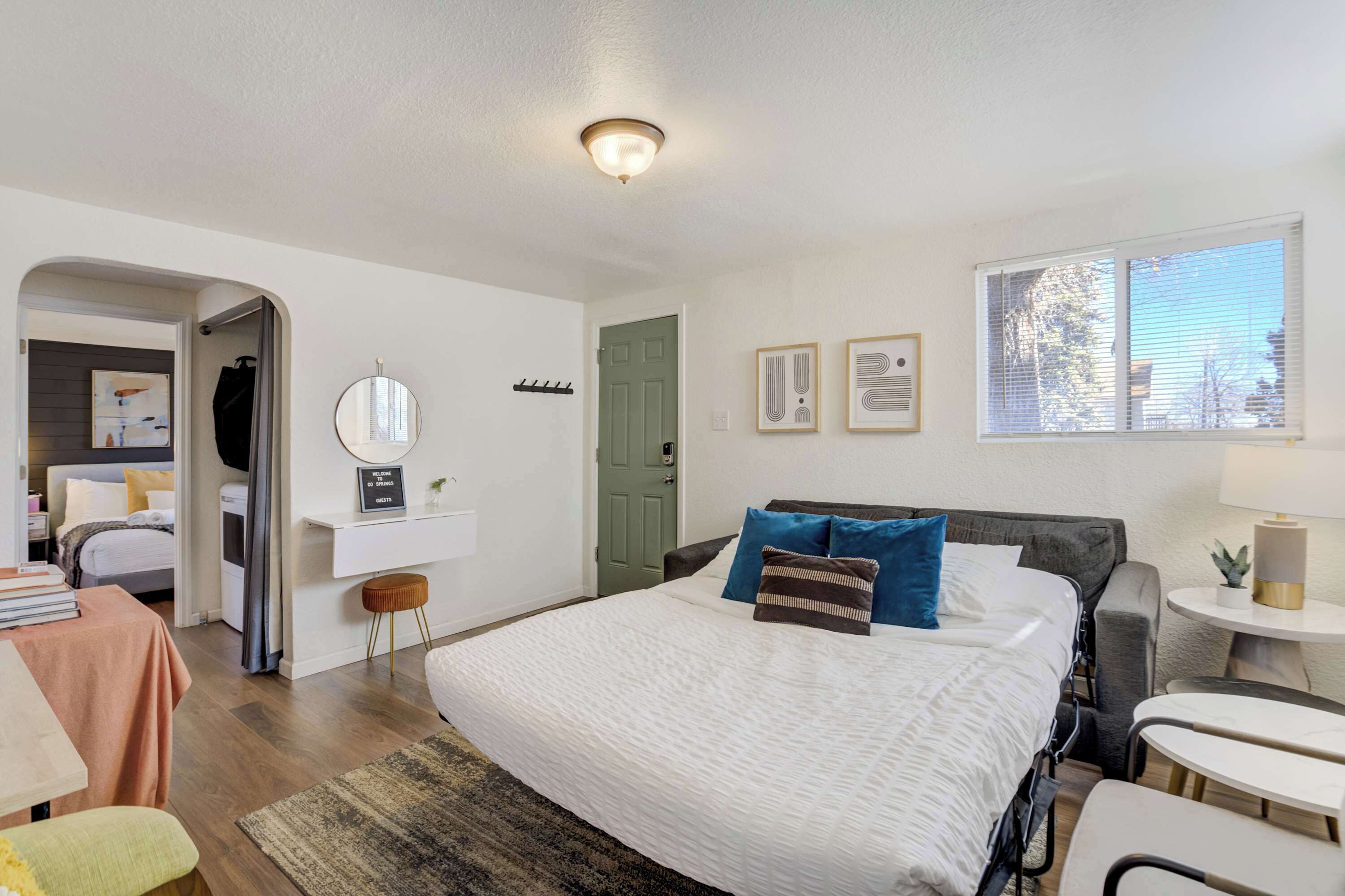 A modern bedroom with a large bed, bedside tables, a desk, and a window with blinds.