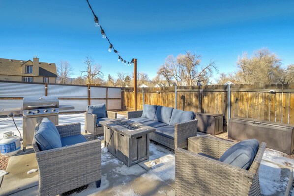 Un patio al aire libre con mobiliario de mimbre, una parrilla y una valla de madera.